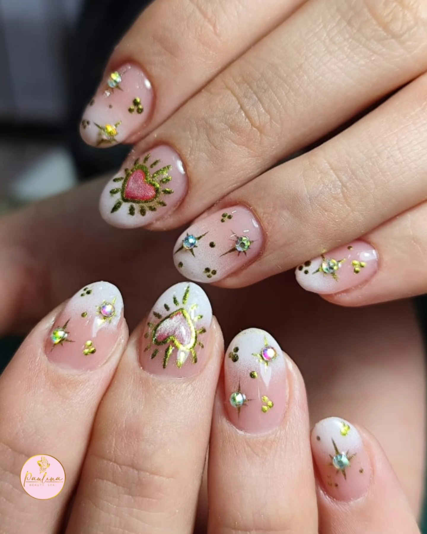 Uñas cortas con degradé nude a blanco, corazones sagrados dorados pintados a mano, estrellas doradas y strass tornasolados