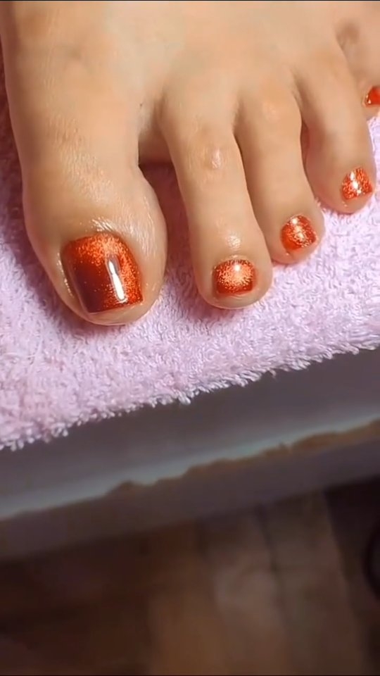 Uñas de los pies en semipermanente cobre con efecto cat eye, sobre una toalla rosa